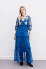 Vestido largo de tul bordado color azul con hilo de lurex y lentejuelas plateadas. Tiene escote en V cruzado, mangas 3/4 con volados y puños elásticos, frunces en la cintura y viso a tono.