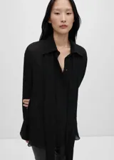 Camisa negra de tejido fluido semitransparente con lazo en el cuello, mangas largas con puños abotonados, diseño recto, cuello camisero, bajo con aberturas laterales y cierre delantero con botones.
