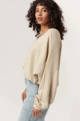 Buzo color beige de corte holgado con cuello redondo y mangas abullonadas. Presenta detalles sin rematar en la parte delantera y trasera, y detalles acanalados en las mangas y el dobladillo.