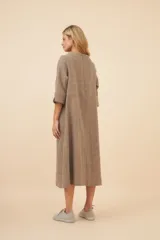 Vestido largo debajo de la rodilla, color marrón claro, con cuello bote, mangas 3/4 y bolsillos laterales. Prenda forrada con tajo en las mangas. Confeccionado en lana fina sin teñir, diseñado exclusivamente por Don Baez.