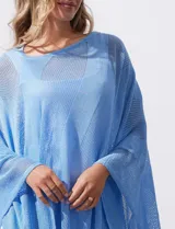 Poncho blanco de tejido calado con lurex, terminación asimétrica y cuello redondo.