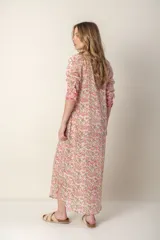 Vestido largo con estampado floral en tonos rosa y verde sobre fondo blanco. Tiene cuello con volantes, cierre frontal con botones y mangas largas con puños elásticos.