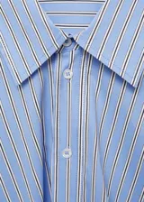 Vestido camisero corto con estampado de rayas verticales celestes y blancas. Tiene cuello camisero, mangas largas con puños abotonados y cierre cruzado con botones.