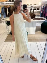 Vestido largo color crema de tejido de punto en hilado fino con lurex. Con una silueta en A, sin manga y de cuello halter. Su tejido a rayas presenta aumentos para brindar soltura y comodidad.