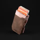 Billetera doble de cuero marrón con detalles en rosa. Cuenta con doble caja de aluminio con sistema de deslizamiento para tarjetas, clip para billetes y espacio adicional para documentos.