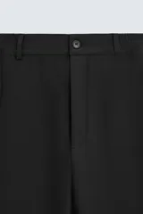 Pantalón negro de corte recto, con cintura elástica y cierre frontal de cremallera y botón. Presenta bolsillos delanteros y bolsillos traseros de vivo.