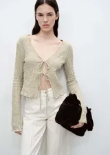 Cárdigan color beige de tejido con textura, corte recto, cuello de pico y cierre frontal con lazos.
