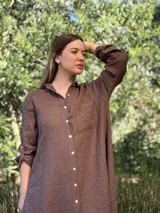 Vestido camisero blanco de lino, con cuello camisero, manga larga con botón para recoger, cierre frontal con botones de nácar, bolsillo en el pecho y diseño asimétrico más largo en la parte trasera.