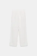Pantalón blanco de tiro medio con pierna ancha y tejido que contiene lino. Presenta cintura con trabillas y un cinturón ajustable con lazada del mismo tejido. Cierre frontal con cremallera y botón.