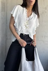 Camisa blanca con cuello en V, mangas cortas con volados y detalle de tablas verticales en el frente.
