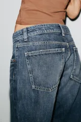 Pantalón de jean celeste claro, de tiro bajo, corte wide leg y largo hasta el tobillo. Tiene cinco bolsillos, cierre frontal con cremallera y botón metálico.