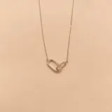 Conjunto de plata 925 con circonias que incluye aros tipo argolla, collar de doble cadena con dijes y pulsera con dijes. Los aros son argollas pequeñas con circonias. El collar tiene una cadena con un dije rectangular y otra cadena con un dije circular. La pulsera tiene un dije con dos círculos entrelazados.
