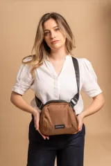 Bandolera pequeña de tela tafeta color marrón, con forma redondeada y correa ancha ajustable de color negro. Presenta un parche rectangular negro con el logo de la marca en el frente.