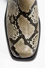 Botas Chelsea de mujer con estampado de piel de serpiente en tonos beige, negro y marrón. Presentan punta y taco cuadrados, elásticos laterales negros y una trabilla trasera para facilitar el calce.