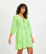 Vestido corto color verde lima con estampado de flores en verde claro, escote en V con lazo, mangas 3/4 con puños elásticos y falda con volantes.