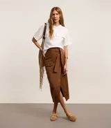 Pollera midi marrón de corte evasé, confeccionada en sarga de algodón. Presenta cintura con trabillas, cinturón con lazo, bolsillo cargo con solapa y encaje delantero.