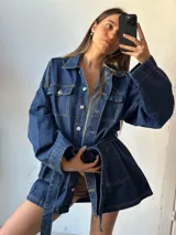 Campera tipo trench de denim azul con cuello clásico, cierre frontal con botones metálicos, bolsillos con solapa en el pecho y cinturón de lazo en la cintura.