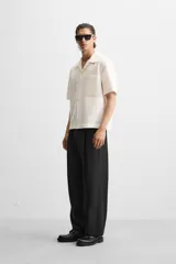 Camisa color blanco con textura de rayas verticales, corte relaxed fit, cuello bowling, manga corta, bolsillo de parche en el pecho y cierre frontal con botones.
