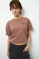Remera de manga corta color marrón, con cuello a la base, inscripción en el frente y gran estampado en la espalda.