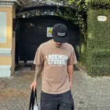 Camiseta oversize marrón con efecto acid wash y estampado frontal blanco con la leyenda "Lookmom Studios".