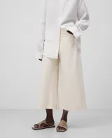 Pantalón cropped de denim de algodón color crudo, con trabillas, cierre con botón metálico, bolsillos delanteros y traseros, y pierna ancha acampanada en el bajo.