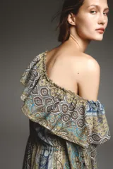 Vestido corto con estampado paisley en tonos ocre, azul y marrón. Tiene escote recto con volantes, mangas largas abullonadas con puños elásticos y cintura elástica.