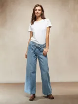 Jean de mezclilla azul claro, tiro alto, con lazo de tela para ajustar la cintura y corte ancho (wide leg). Presenta costuras verticales marcadas en el frente de ambas piernas.
