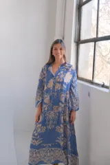 Vestido largo celeste con estampado floral en tonos beige, corte amplio, cuello camisero y mangas largas.