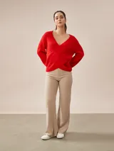 Buzo de tejido de punto rojo, con escote en V cruzado tipo wrap y mangas largas abullonadas con puños ajustados.