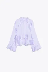 Camisa lila de cuello redondo y manga larga con volantes en el mismo tejido. Cierre en la espalda con aberturas y botones.
