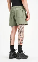 Short de baño verde militar de calce regular, con elástico en la cintura, cordón de ajuste con inscripción "LUXURY" y tres bolsillos.