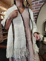 Chal tejido a mano en lana merino color crudo, con flecos y borde tejido en marrón oscuro. Diseño con textura de canasta y etiqueta de cuero grabada.