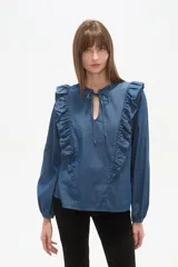 Blusa blanca de calce holgado con cuello en V y lazo frontal. Presenta detalles de volados en el pecho y cuello, y mangas largas con puños elásticos.