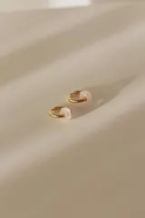 Par de aros tipo argolla dorados con dije de piedra natural con patrón de manchas negras sobre fondo blanco.