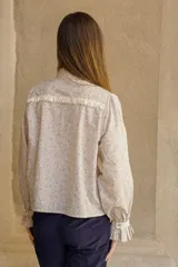 Camisa de algodón con estampado floral, cuello clásico, cierre frontal con botones, mangas largas con puños fruncidos y detalle de puntilla en puños y espalda.