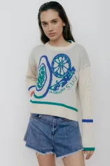 Buzo color crudo con diseño jacquard de frutas y verduras en azul y verde. Mangas largas tejidas en ochos con puños con agujero para el dedo.