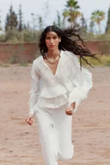 Camisa blanca de cuello redondo con escote en V y mangas largas acampanadas con volantes.