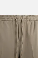 Pantalón color arena de corte recto, confeccionado en tejido elástico. Cuenta con cintura elástica ajustable con cordón, bolsillos laterales y bolsillos de vivo en la parte trasera.