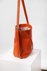 Bolso tipo bucket de cuero color marrón con costuras a la vista, doble bolsillo interior (uno con cierre) y correa regulable.