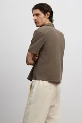 Camisa marrón de punto con textura, corte regular, cuello inglés, tapeta lisa, canesú en la espalda, bajo recto con aberturas laterales y manga corta.