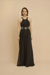 Vestido largo de fiesta negro, con cuello halter, espalda descubierta y falda de gasa. Presenta un aplique de pedrería en la cintura.