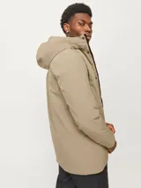 Parka larga color beige con capucha ajustable, cierre frontal con solapa cortaviento, bolsillos funcionales y puños de canalé.