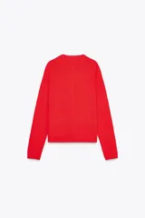 Chaqueta roja de punto con cuello redondo y manga larga. Tiene bolsillos delanteros de plastrón, cierre frontal con botones dorados con relieve y acabados en rib.