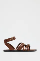 Sandalias planas de cuero color marrón con tiras finas y hebillas doradas.