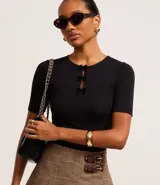 Blusa negra de mangas cortas, confeccionada en Rib, con cuello redondo con lazos de terciopelo uniendo la abertura en la parte de abajo.