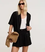 Short blanco de corte runner evasé, con cintura elástica fruncida y un botón decorativo. Presenta bolsillos laterales y un calce suelto.