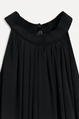 Vestido midi negro de cuello halter y hombros descubiertos. Cintura con elástico, detalle de drapeado lateral y bajo asimétrico. Cierre en cuello con botones.