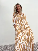 Vestido camisero largo con estampado de cebra en tonos beige y blanco, con cuello camisero, mangas largas con puños abotonados y cierre frontal con botones.