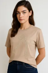 Remera color beige de manga corta con cuello redondo y aplique de lazo bordado en el frente.