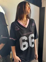 Remerón negro con cuello en V y ribete rosa, mangas cortas con rayas blancas y rosas, y estampado frontal con el texto "Lucky Feeling" y el número "66" en blanco.